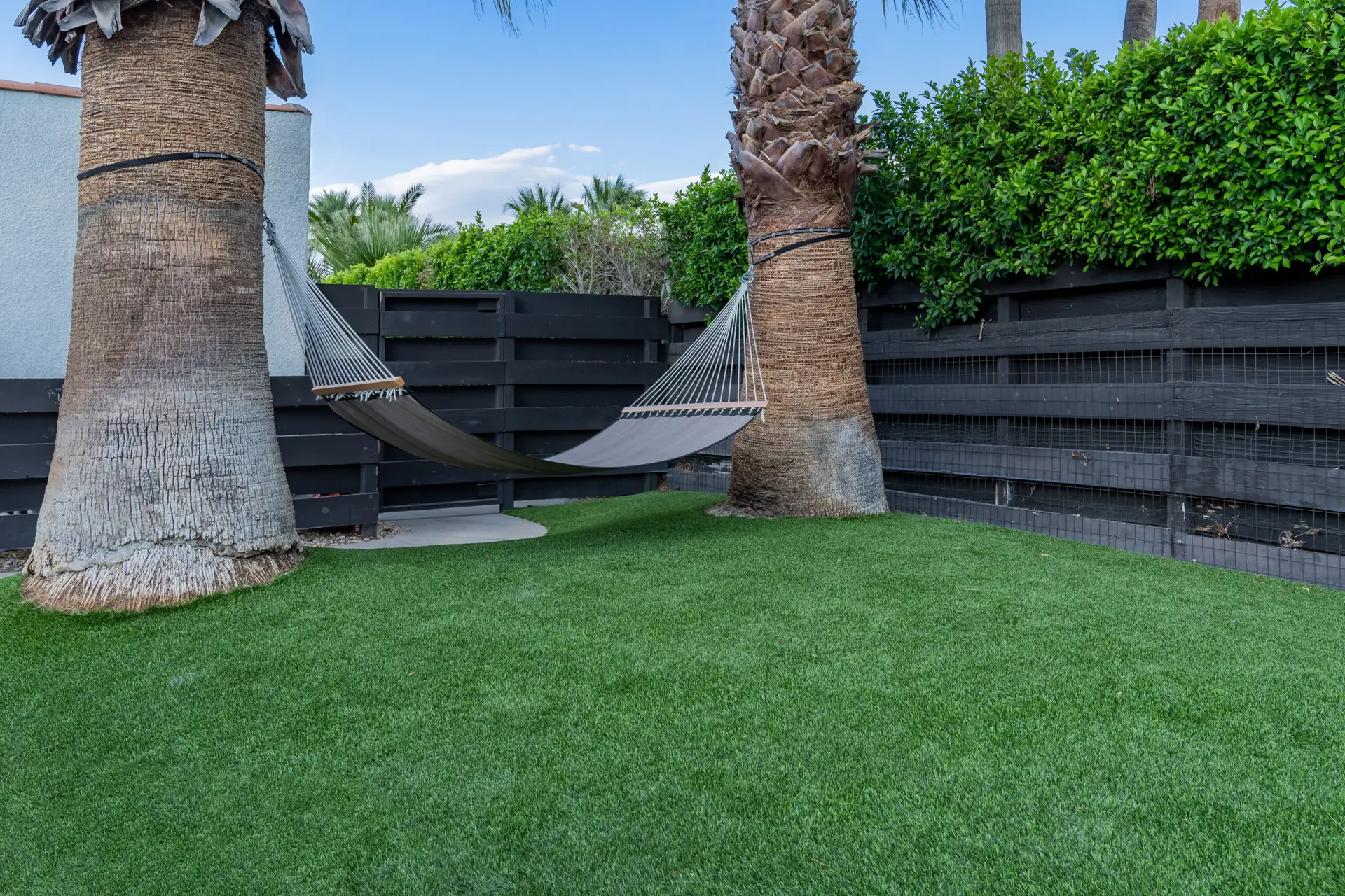 Backyard with a hammock suspended between two palm trees over clean, well-maintained artificial turf.
