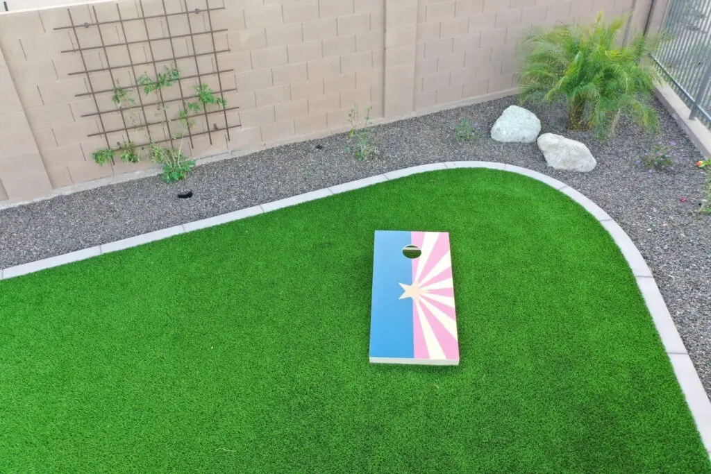 Artificial turf backyard with a cornhole board and desert landscaping