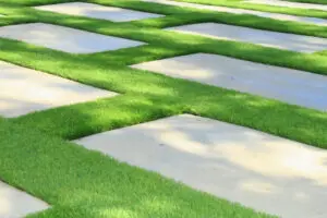 Modern concrete paver walkway bordered by clean, professionally maintained artificial turf in a landscaped residential yard.