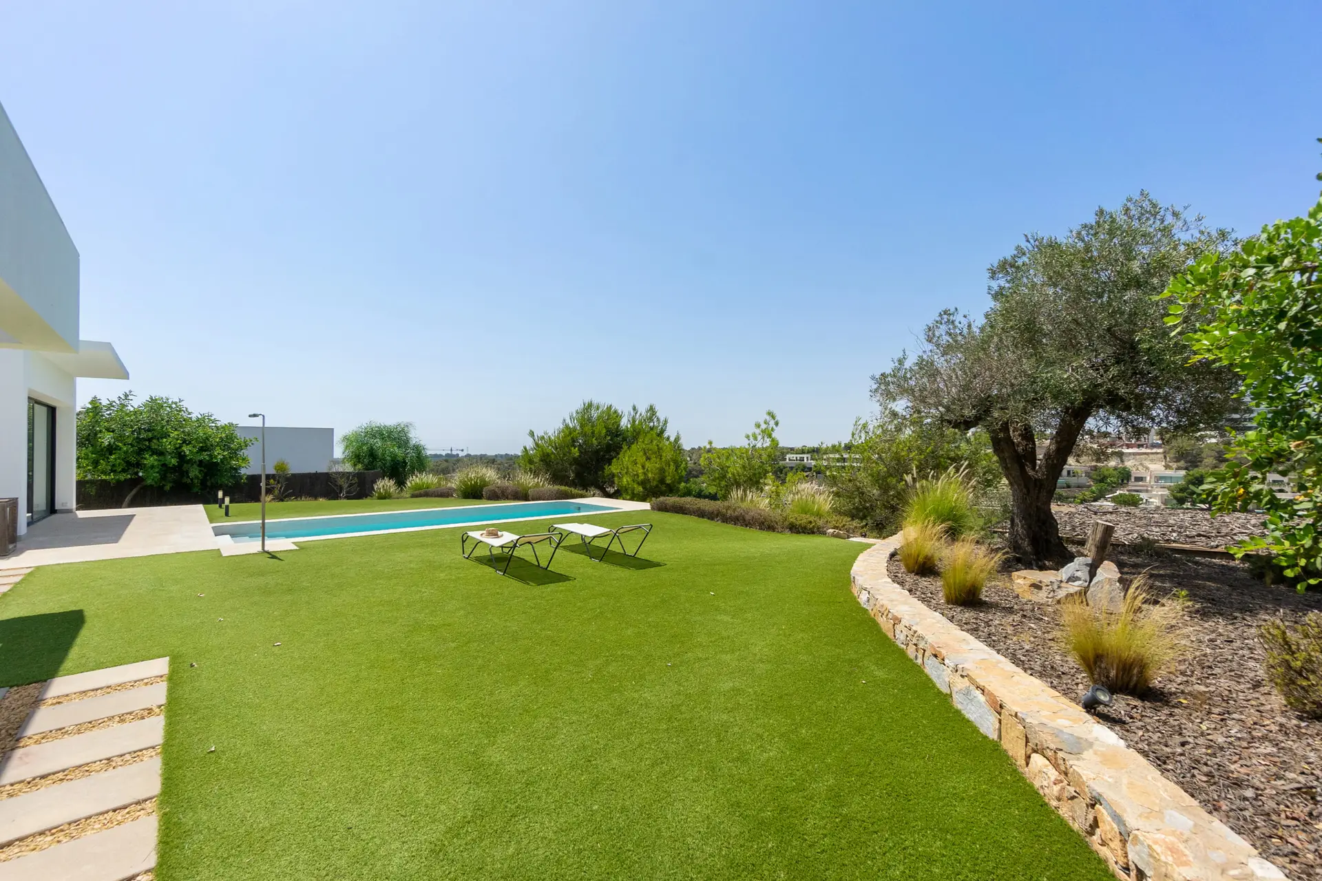 Modern backyard featuring a swimming pool, landscaped garden, and professionally maintained artificial turf lawn.